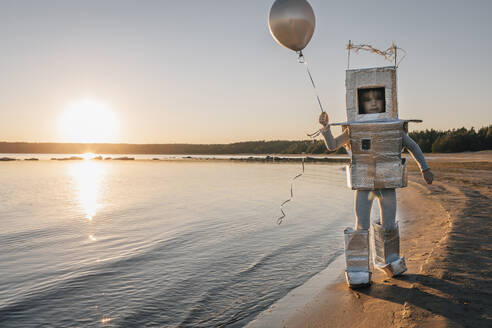 Junge im Astronautenanzug und mit Luftballon am Strand bei Sonnenuntergang - EVKF00025