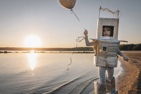 Junge im Astronautenkostüm und mit Luftballon am Strand bei Sonnenuntergang - EVKF00026