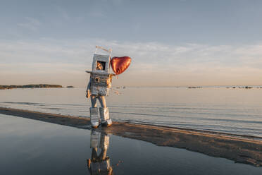 Junge im Astronautenanzug mit herzförmigem Ballon am Strand bei Sonnenuntergang - EVKF00027