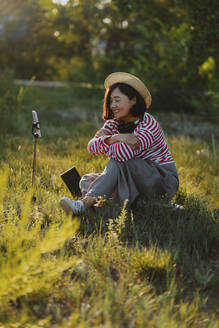 Smiling woman recording vlog on smart phone in field - IEF00496