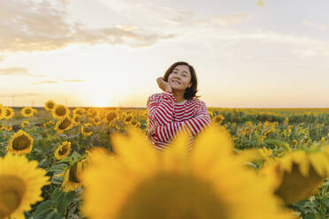 Reife Frau inmitten von Sonnenblumen auf einem Feld - IEF00517