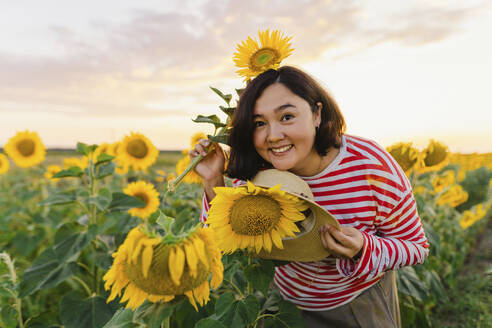 Glückliche Frau mit Hut in einem Sonnenblumenfeld - IEF00521