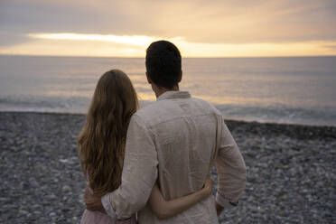 Junger Mann und Frau, die sich umarmen und das Meer am Strand genießen - YBF00173