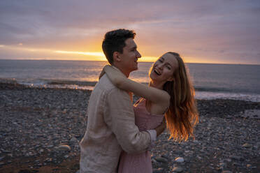 Glückliches junges romantisches Paar tanzt am Strand bei Sonnenuntergang - YBF00181