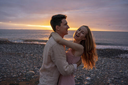 Glückliches junges romantisches Paar tanzt am Strand bei Sonnenuntergang - YBF00181