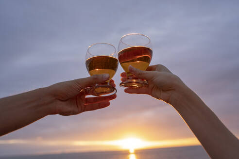 Hände von Freundin und Freund stoßen mit Weingläsern bei Sonnenuntergang an - YBF00182