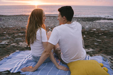 Lächelndes junges romantisches Paar im Gespräch am Strand im Urlaub - YBF00183