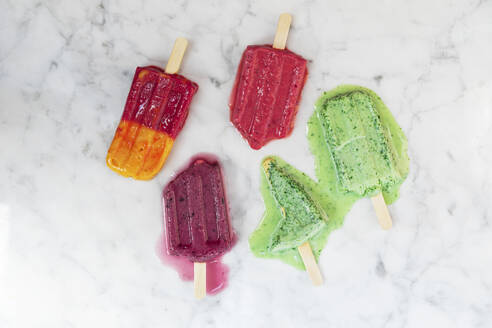 Homemade berry fruit popsicles melting against marble surface - GWF07901