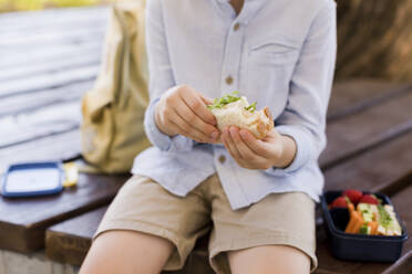 Boy holding sandwich sitting on bench - ONAF00630