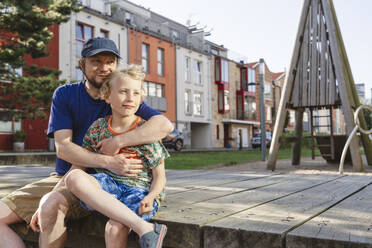 Nachdenklicher Vater, der seinen Sohn auf dem Spielplatz umarmt - IHF01616