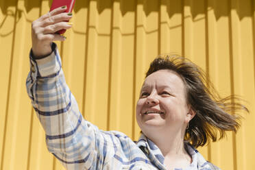 Smiling woman taking selfie with smart phone on sunny day - OSF02067