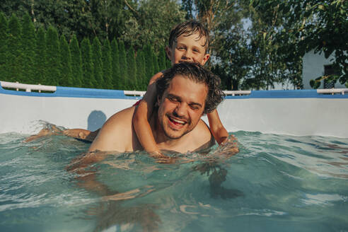 Glücklicher Vater trägt seinen Sohn auf dem Rücken in den Pool - VSNF01378