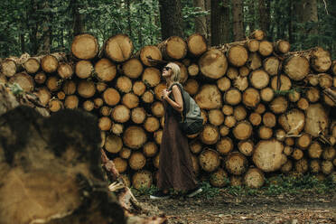 Woman with backpack walking by wood logs in forest - VSNF01382