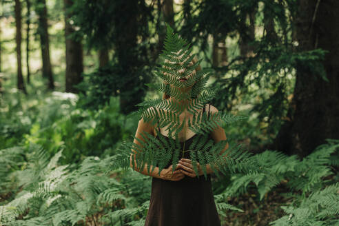 Woman hiding behind fern leaf in forest - VSNF01386
