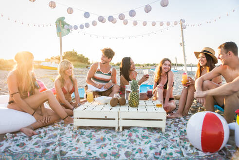 Eine Gruppe von Freunden macht ein Picknick am Strand - Glückliche junge Leute im Sommerurlaub am Strand - DMDF03979