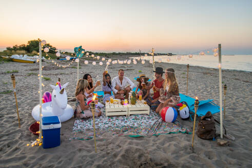 Eine Gruppe von Freunden macht ein Picknick am Strand - Glückliche junge Leute im Sommerurlaub am Strand - DMDF04035