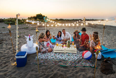 Eine Gruppe von Freunden macht ein Picknick am Strand - Glückliche junge Leute im Sommerurlaub am Strand - DMDF04037