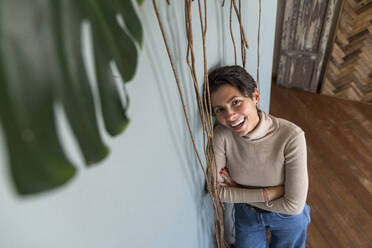 Smiling woman with arms crossed leaning on wall at home - VPIF08557