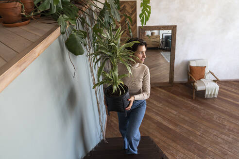 Lächelnde Frau, die eine Pflanze hält und eine Treppe hinaufgeht - VPIF08558