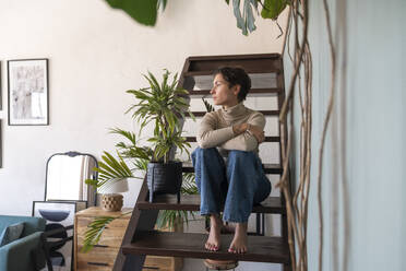 Thoughtful woman with arms crossed sitting on staircase at home - VPIF08563
