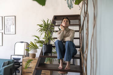 Lächelnde Frau auf der Treppe sitzend mit Pflanze zu Hause - VPIF08564