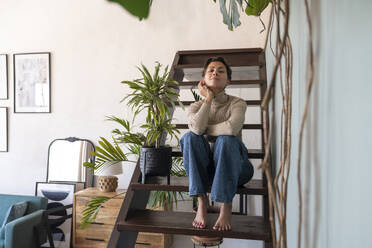 Smiling woman sitting on staircase with plant at home - VPIF08564