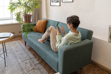 Woman with short hair sitting on sofa and using smart phone at home - VPIF08594