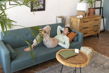 Lächelnde Frau entspannt sich auf dem Sofa zu Hause - VPIF08598