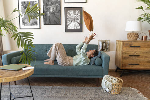 Fröhliche Frau gestikuliert und entspannt auf dem Sofa zu Hause - VPIF08602