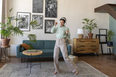 Glückliche Frau mit drahtlosen Kopfhörern tanzt im Wohnzimmer zu Hause - VPIF08606
