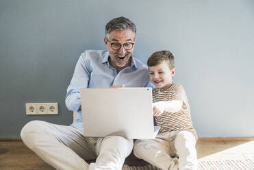 Cheerful grandfather and grandson using laptop at home - UUF29979