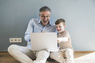 Fröhlicher Großvater und Enkel benutzen Laptop zu Hause - UUF29979