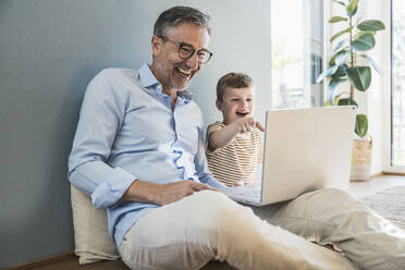 Glücklicher Großvater benutzt Laptop mit Enkel im Wohnzimmer - UUF29980