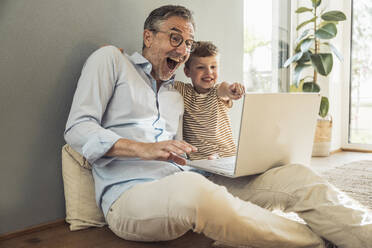 Glücklicher Großvater und Enkel genießen die Nutzung des Laptops zu Hause - UUF29983