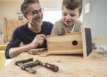 Glücklicher Großvater baut mit seinem Enkel zu Hause ein Vogelhaus aus Holz - UUF29993