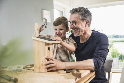Fröhlicher Junge beim Bau eines Vogelhauses durch seinen Großvater zu Hause - UUF29996