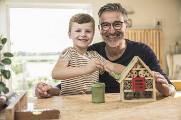 Lächelnder Junge malt Holzhaus von Großvater im Wohnzimmer - UUF30000