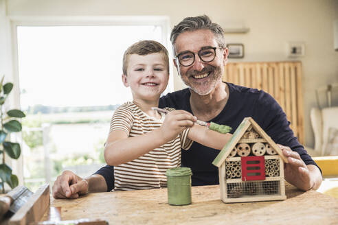 Happy grandson painting model house by grandfather at home - UUF30001