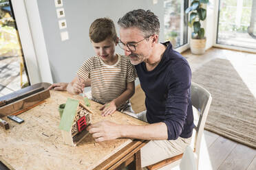 Junge malt Modellhaus von Großvater auf Tisch zu Hause - UUF30003