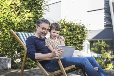 Man sharing tablet PC with grandson in back yard - UUF30009