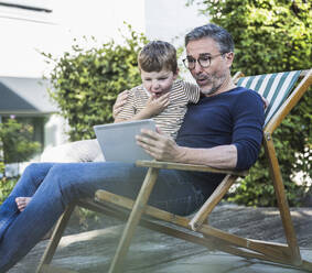 Surprised man and boy using tablet PC at back yard - UUF30011