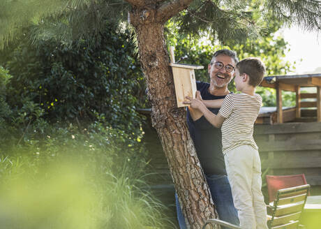 Glücklicher Großvater, der seinem Enkel hilft, das Vogelhaus auf dem Baum auszurichten - UUF30028