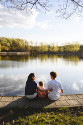 Mutter mit Tochter und Sohn sitzen am See im Park - EYAF02740