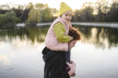 Bruder trägt Schwester auf den Schultern am See im Park - EYAF02745