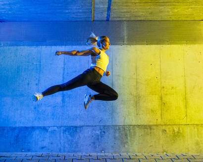 Woman jumping in front of neon colored wall - STSF03759