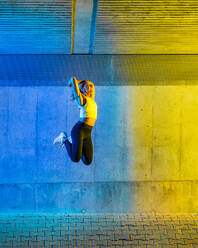Aktive Frau, die vor einer neonfarbenen Wand springt - STSF03760