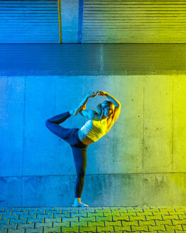 Woman doing yoga in front of neon colored wall - STSF03763