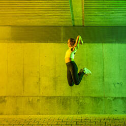 Frau springt in der Nähe einer neonfarbenen Wand - STSF03766