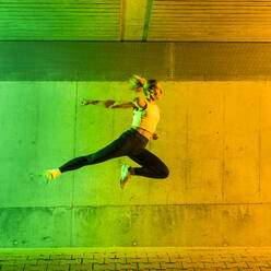 Frau in Sportkleidung springt in der Nähe einer neonfarbenen Wand - STSF03767