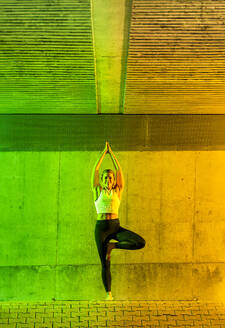 Smiling woman doing yoga in front of neon colored wall - STSF03768